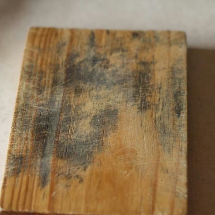 An old wooden cutting board showing dark mould stains in the grain